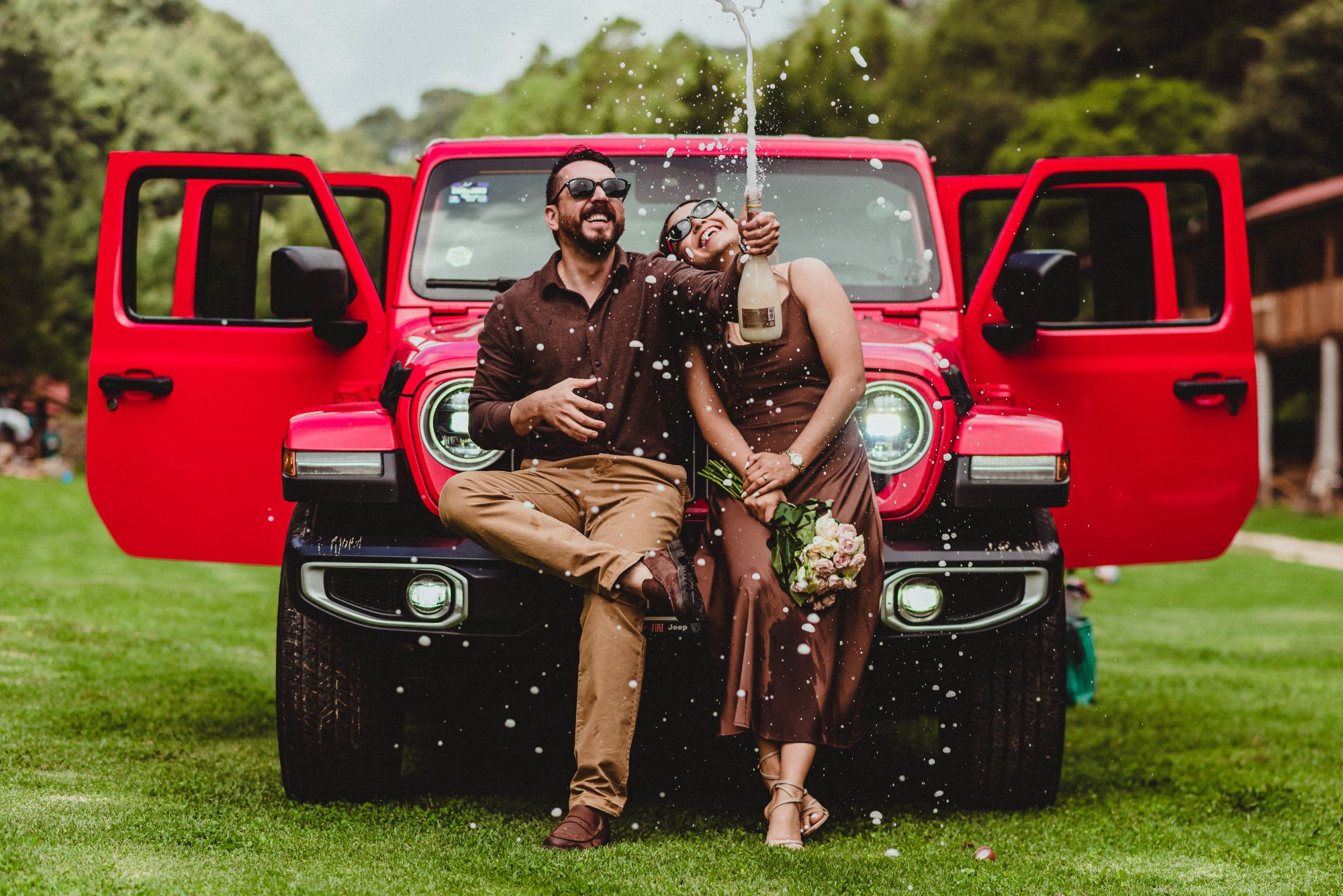 Lupita y Alex brindando frente a un Jeep rojo